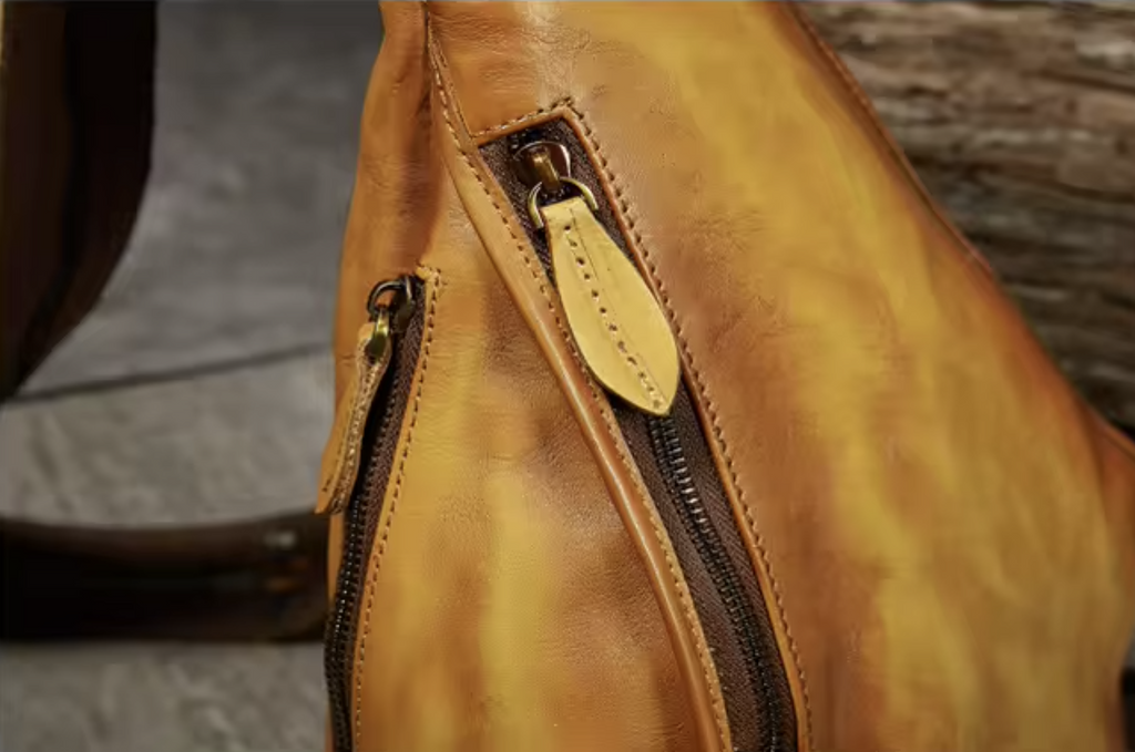 Close-up of a tan leather bag showing a dark zipper with a matching leather pull tab and a smaller side zipper.
