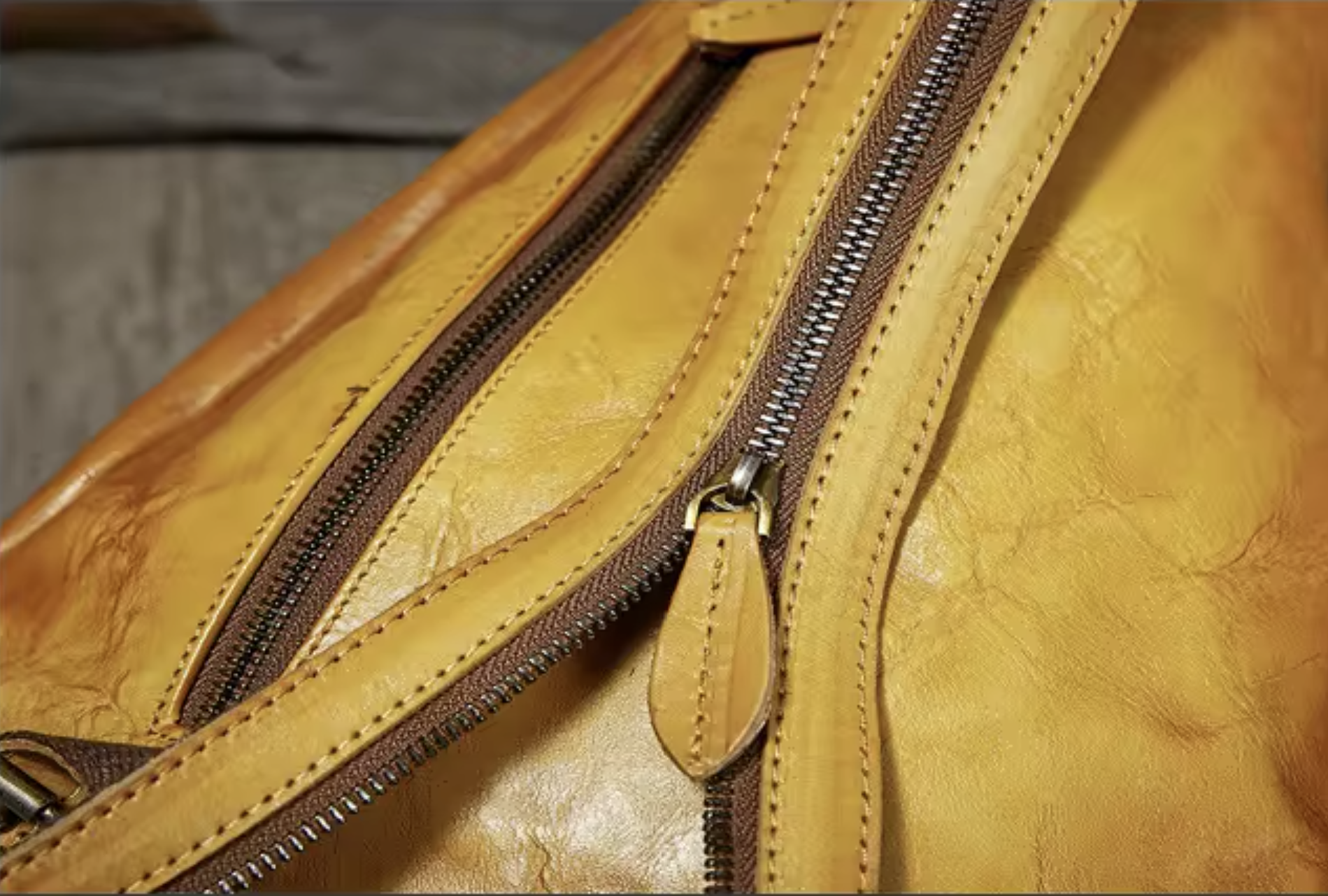 Close-up of a tan leather bag with two diagonal zippers, showing the textured leather material and dark metal zipper teeth.
