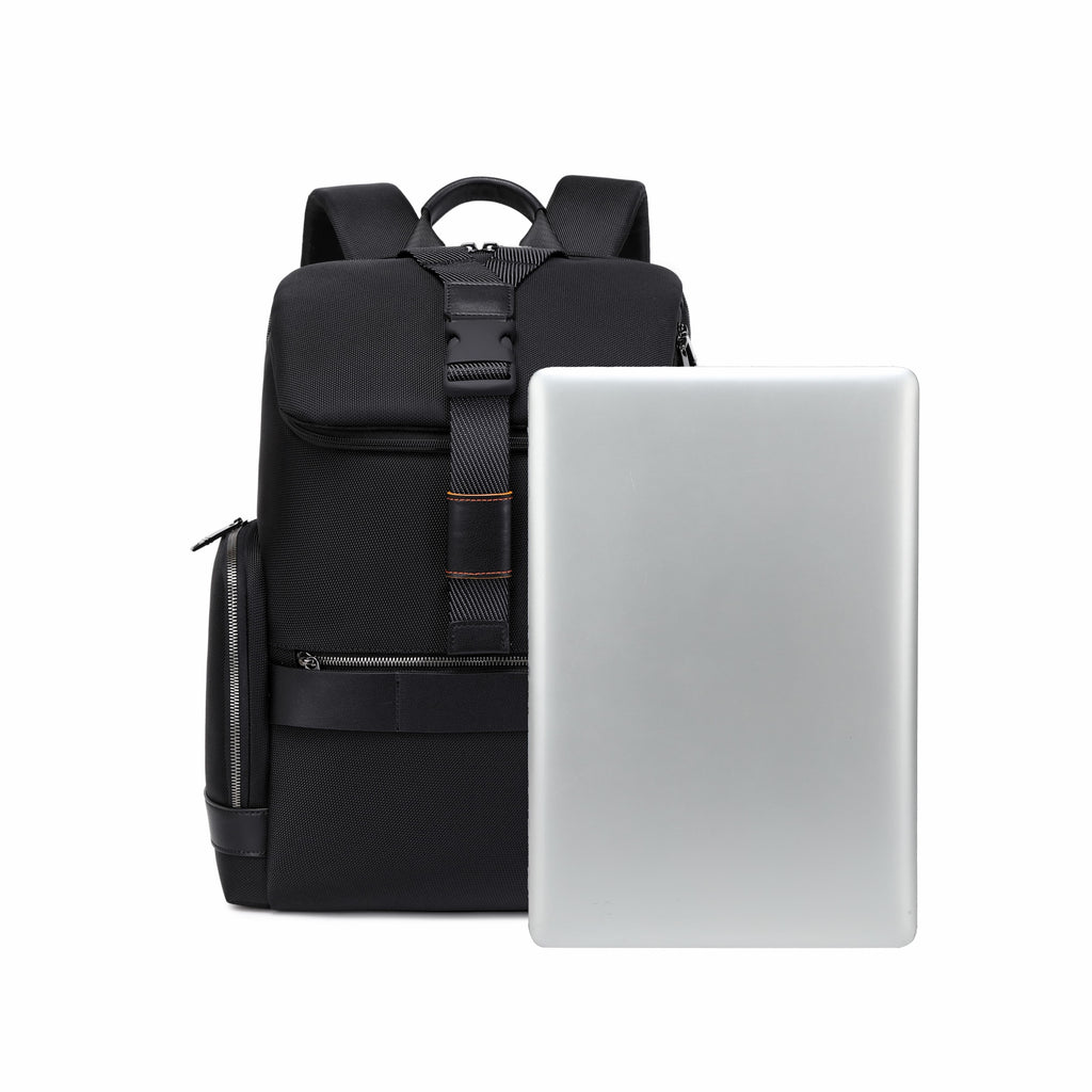 A black backpack standing upright next to a closed silver laptop on a plain white background.