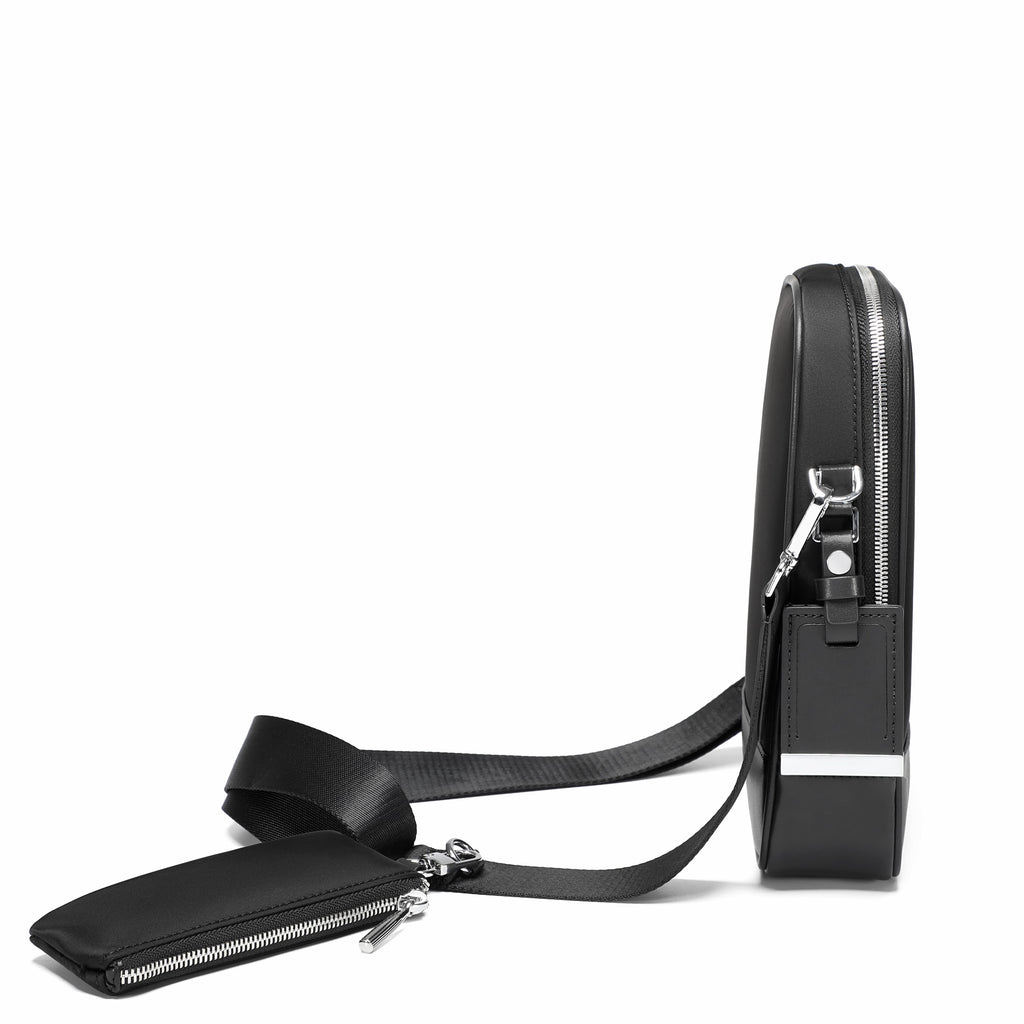 A black leather crossbody bag shown from a side profile view on a clean white background, featuring a matching zippered pouch attached to the strap.