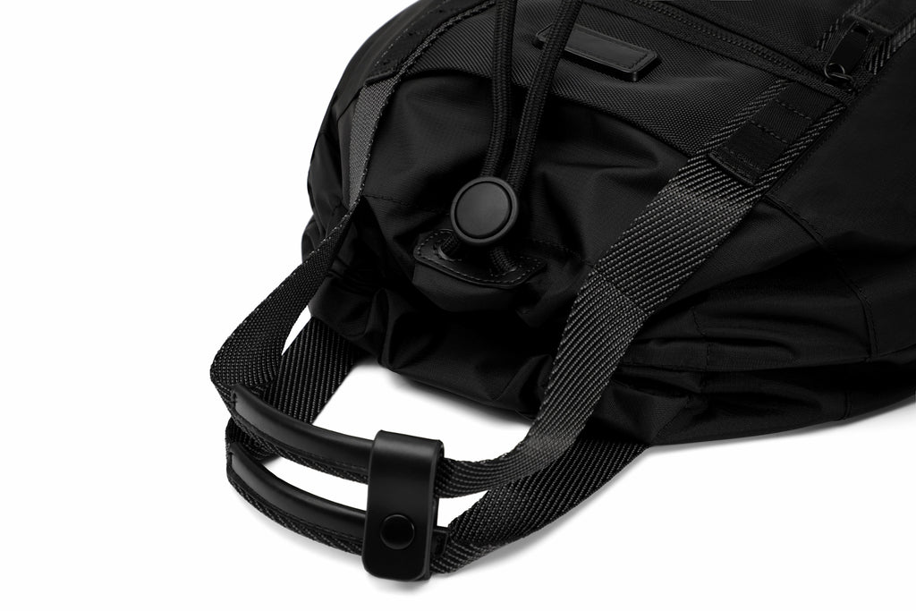 Close-up of a black nylon bag with a black webbing strap and black plastic buckle, photographed on a white background.