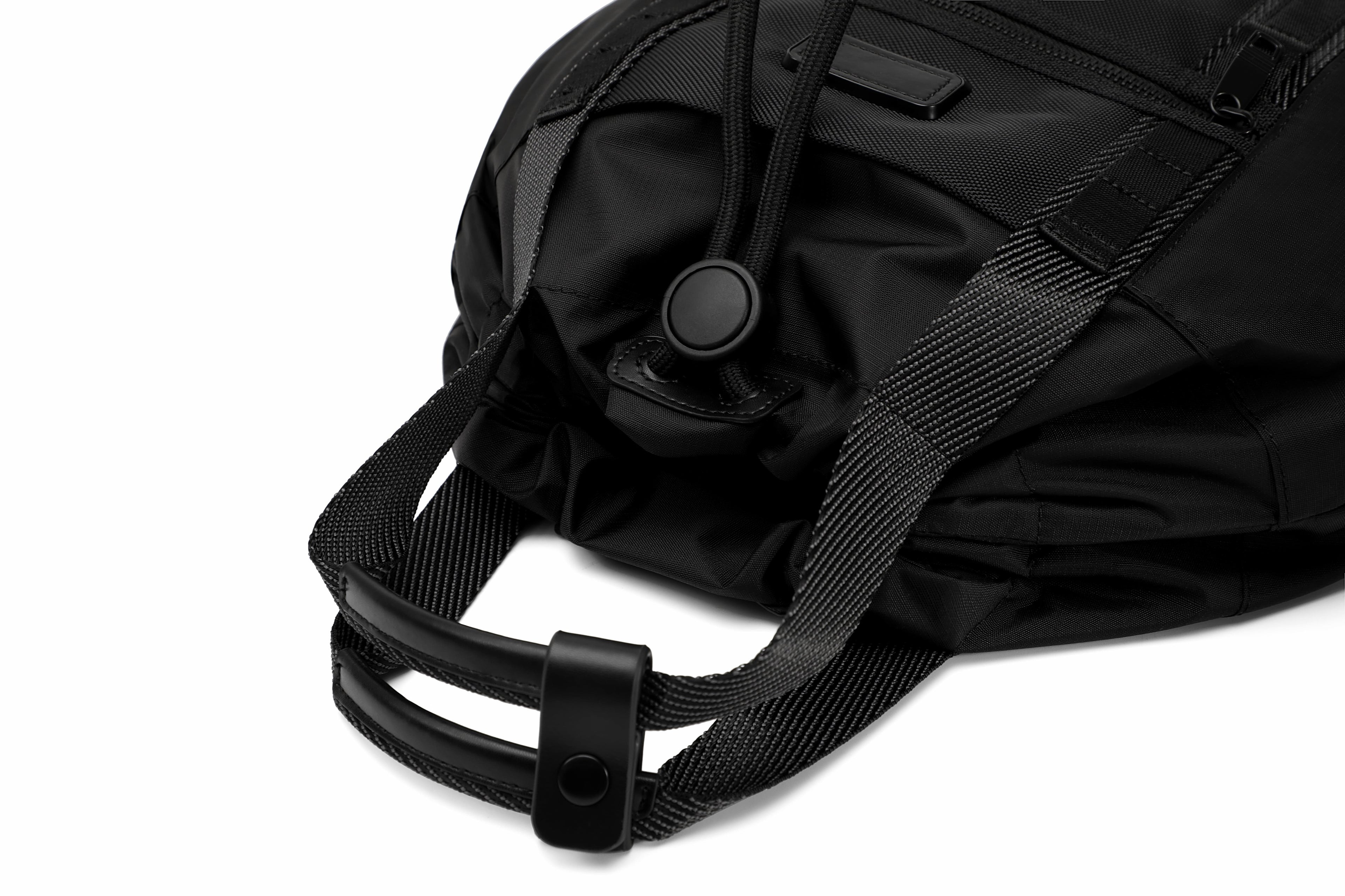 Close-up of a black nylon bag with a black webbing strap and black plastic buckle, photographed on a white background.