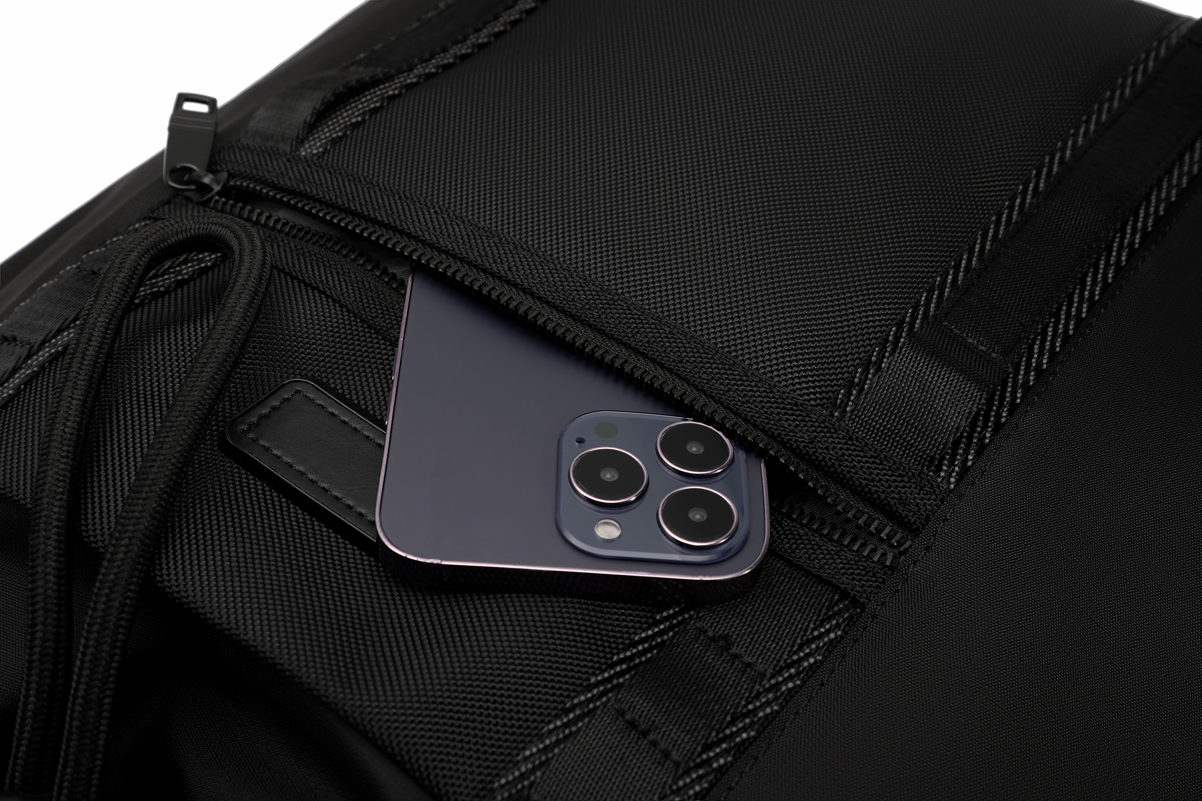 Close-up of a black textured backpack or bag with a zip pocket, showing a dark blue smartphone partially tucked inside.