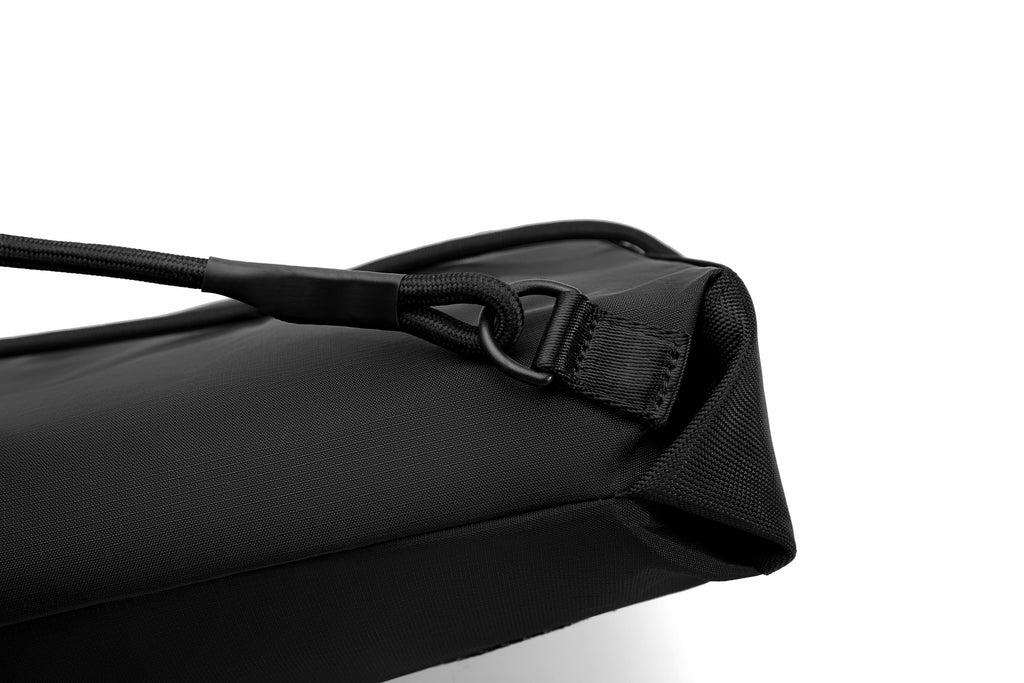 Close-up of a black nylon bag corner with a black strap and hook-and-loop closure, photographed on a white background.